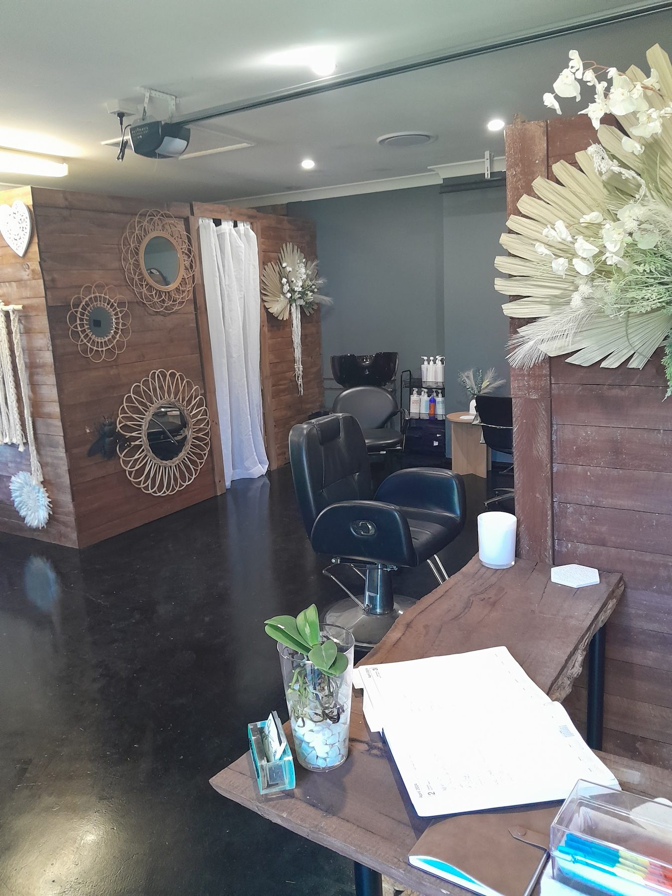 The studio from the front desk: timber desk with an orchid, a styling chair and the wash basin behind